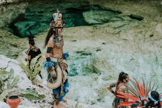 A group of people in traditional Mayan attire perform a cultural ceremony beside a crystal-clear cenote.