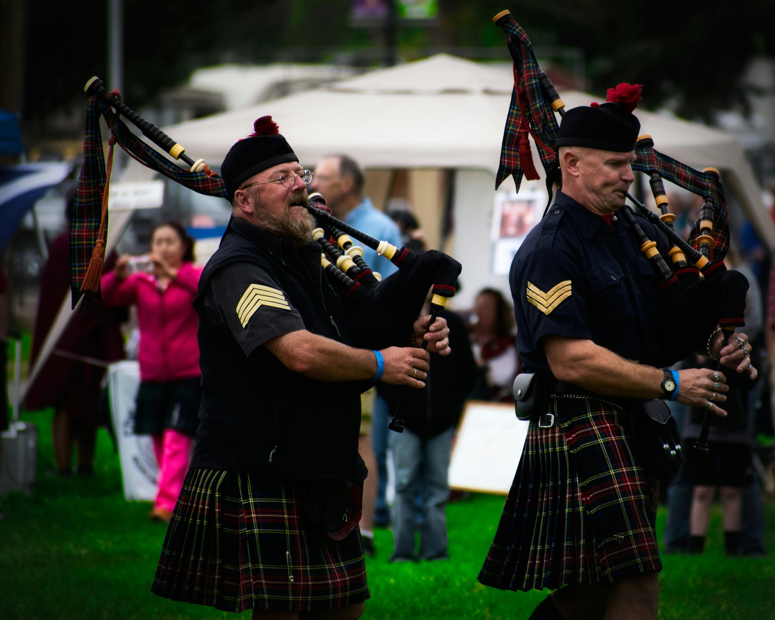 Scottish bagpipers in kilts performing at an outdoor festival.